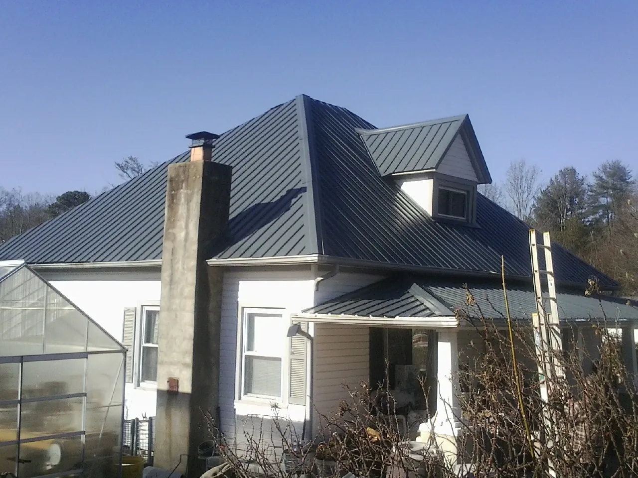 Dark blue standing seam metal roof on a white farmhouse with dormer — Slate & Tile Roof Repair by Roofing Brothers in Evant