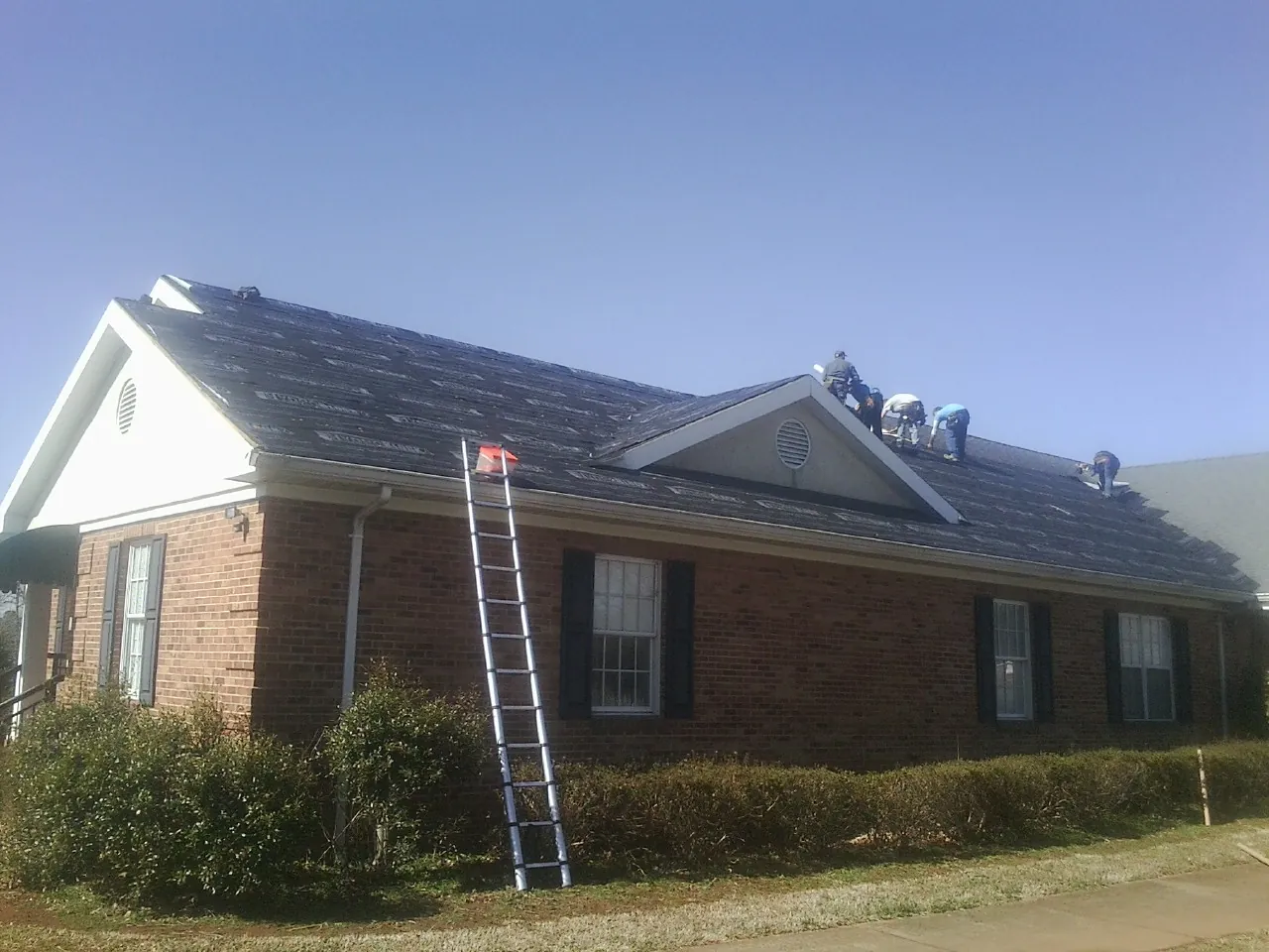 Crew tearing shingles off a brick ranch roof with a ladder set — Metal Roof Repair work by our crew in Evant