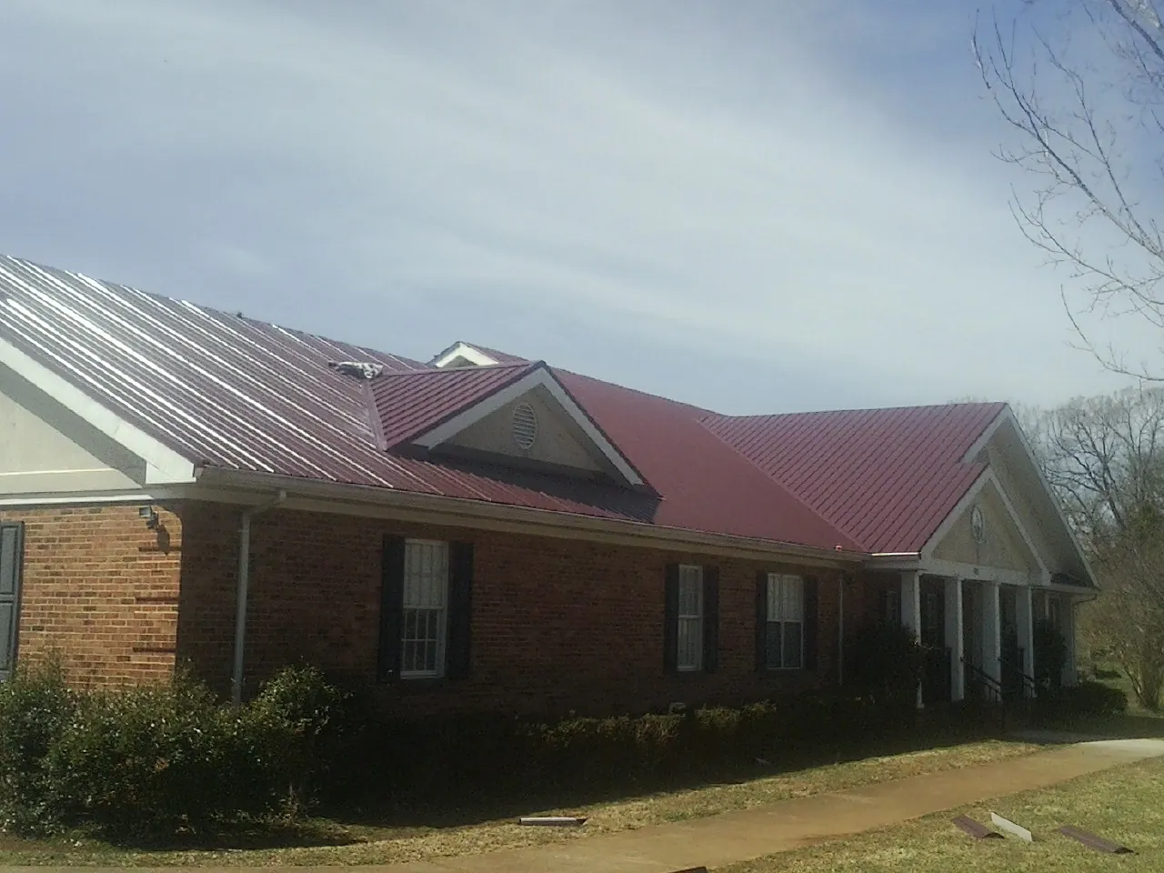 Red metal roof with gabled entries on a long brick building, from a Hail Damage Roof Repair job in Evant