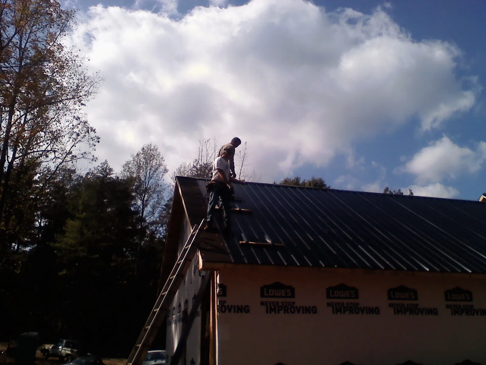 Roofer fastening dark metal panels high against a cloudy sky, from a Roof Inspection job in Evant